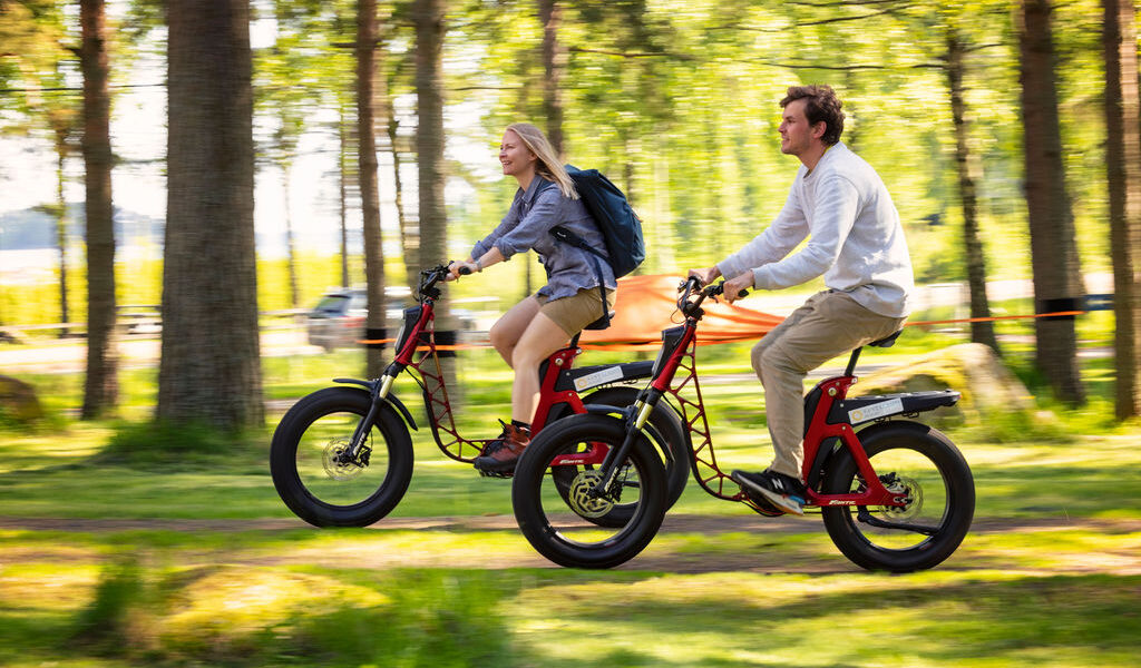 Sähköpolkupyörä vuokraus nainen ja mies ajaa polkupyörillä nurmikolla ja hiekkatiellä - Santalahti Resort - Kotka Finland